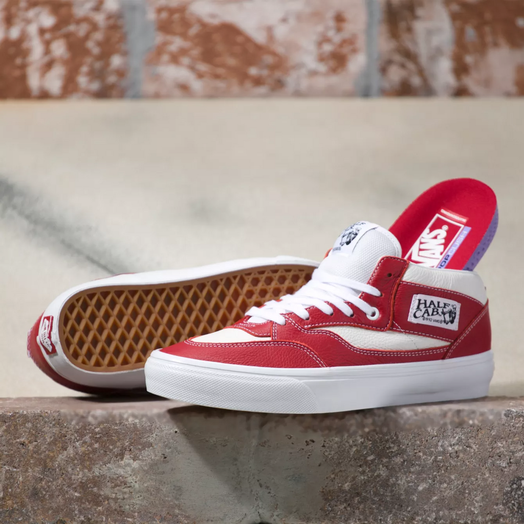 A pair of red VANS LEATHER SKATE HALF CAB '92 CHILI PEPPER / WHITE sneakers on a brick wall.
